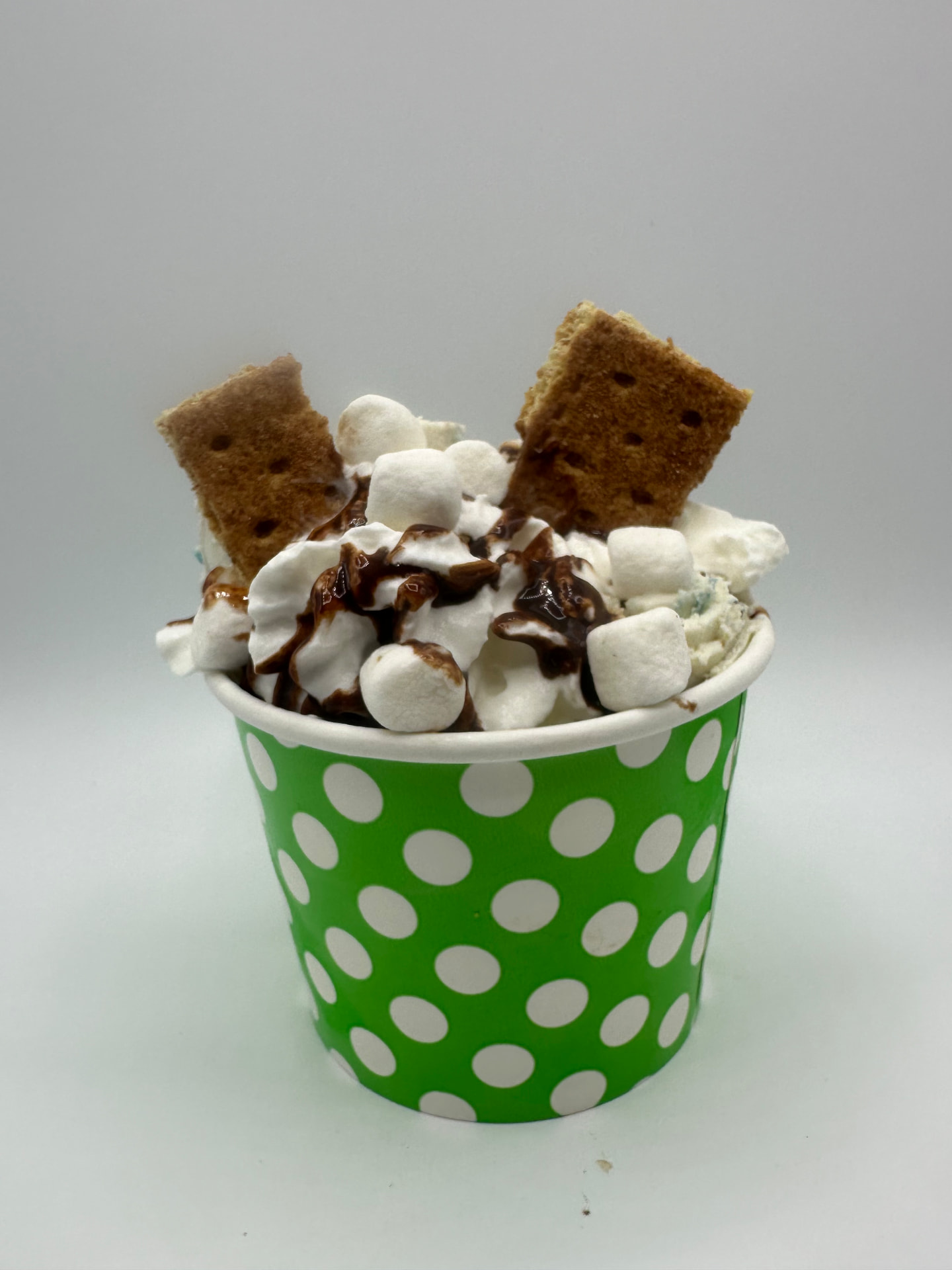 S'more S'mores rolled ice cream in a green polka-dot cup with marshmallows, graham crackers and chocolate drizzle