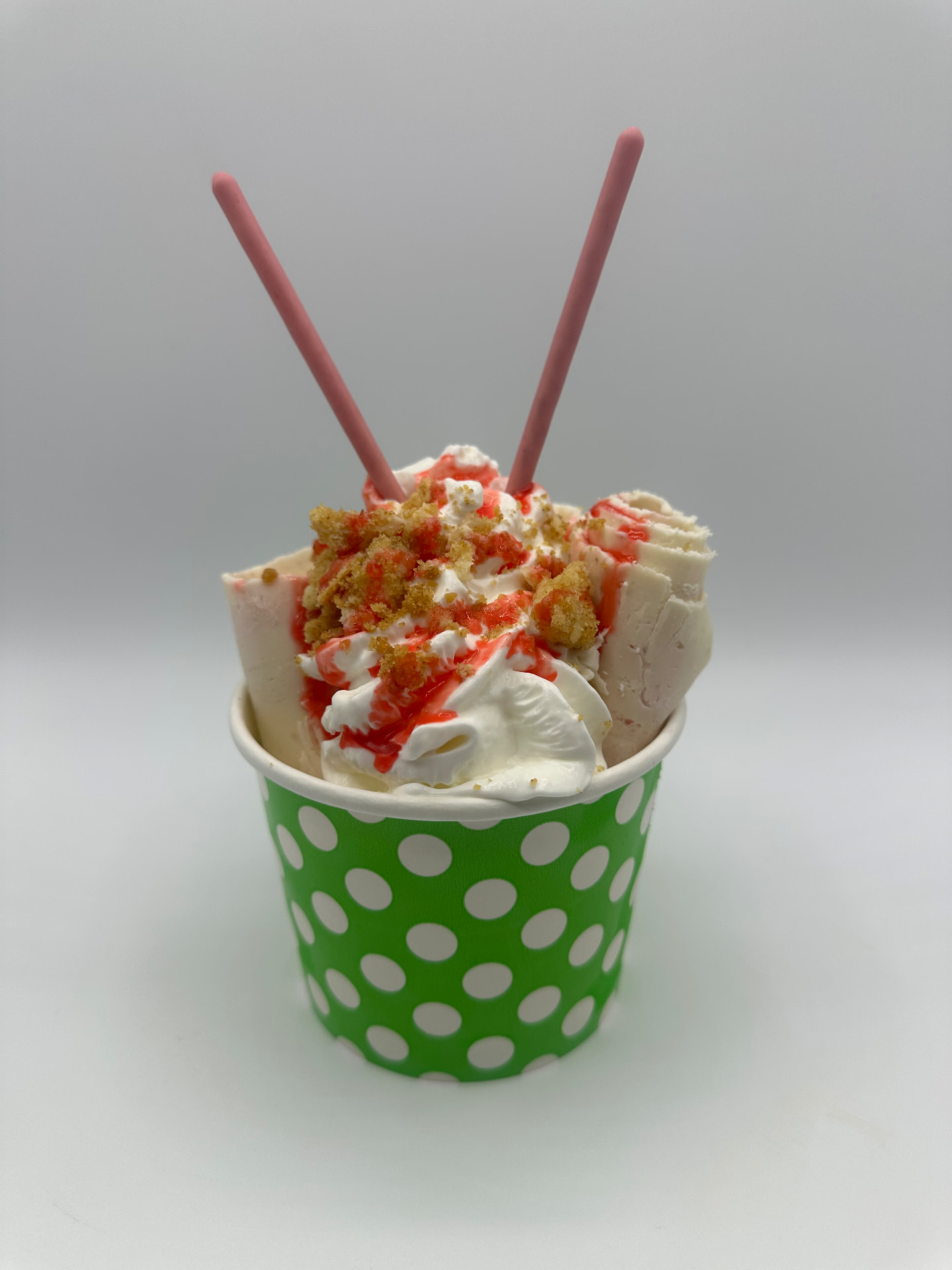 Strawberry Kiss rolled ice cream in a green polka-dot cup with strawberry drizzle, crumble and pink wafer straws