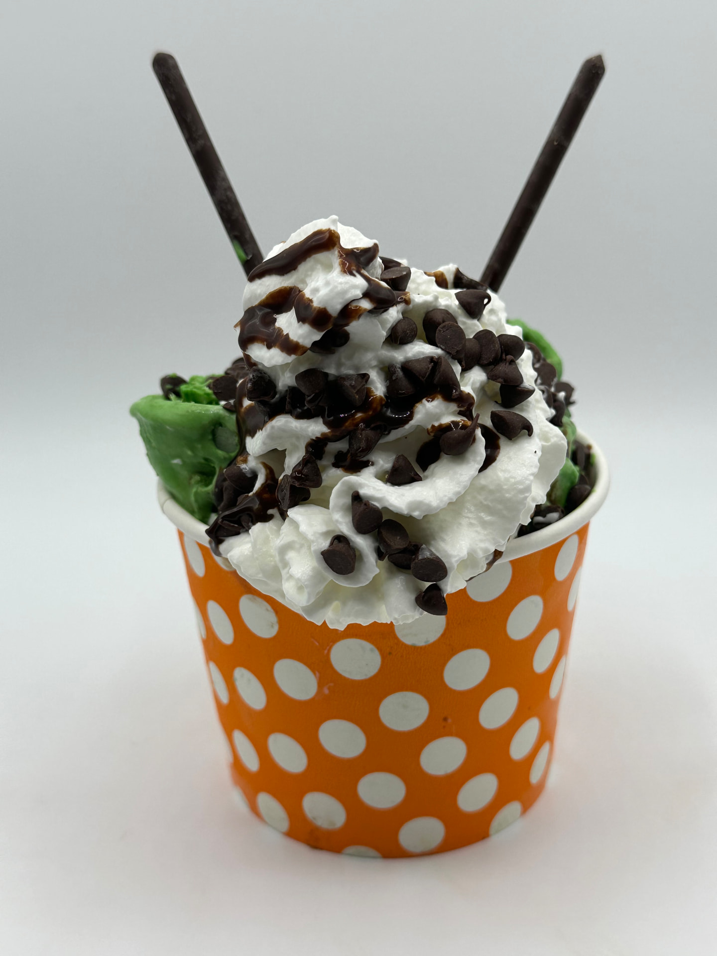 Mint to Be rolled ice cream in an orange polka-dot cup with whipped cream, chocolate chips and fudge drizzle
